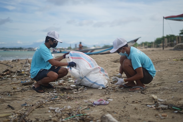 Two men on a beach cleanup gathering plastic and garbace in a bag.