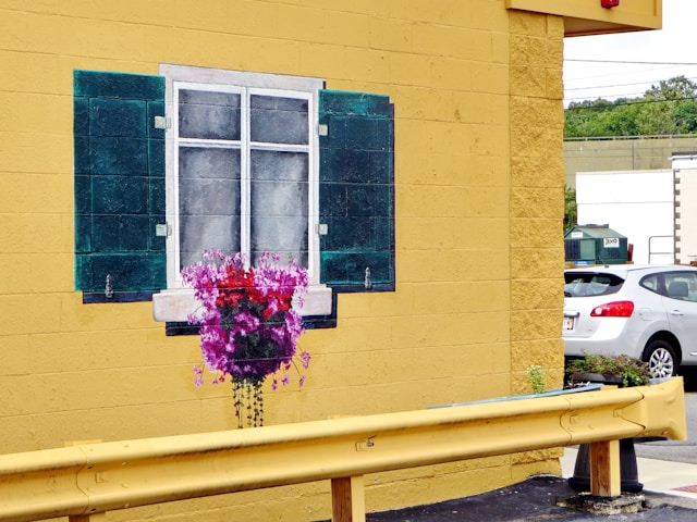 A yellow painted wall of a house with a painted window on the bricks. 