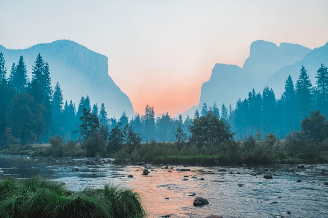 A natural landscape with a flowing river and a setting sun. 